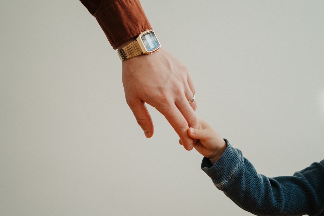 Adult hand holding a child's hand, wearing watches.